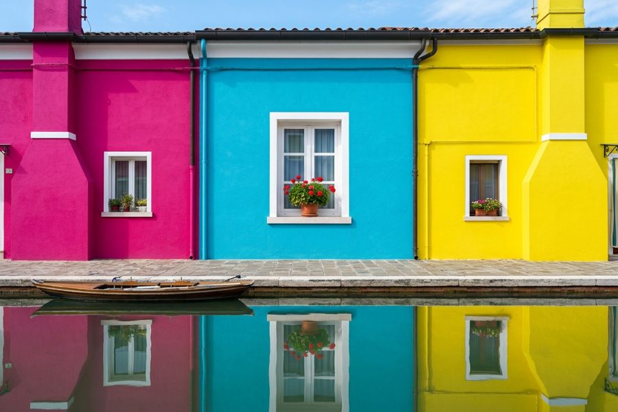 A highly graphic and saturated photograph of adjacent fuchsia, turquoise, and lemon-yellow houses in Burano, Venice.